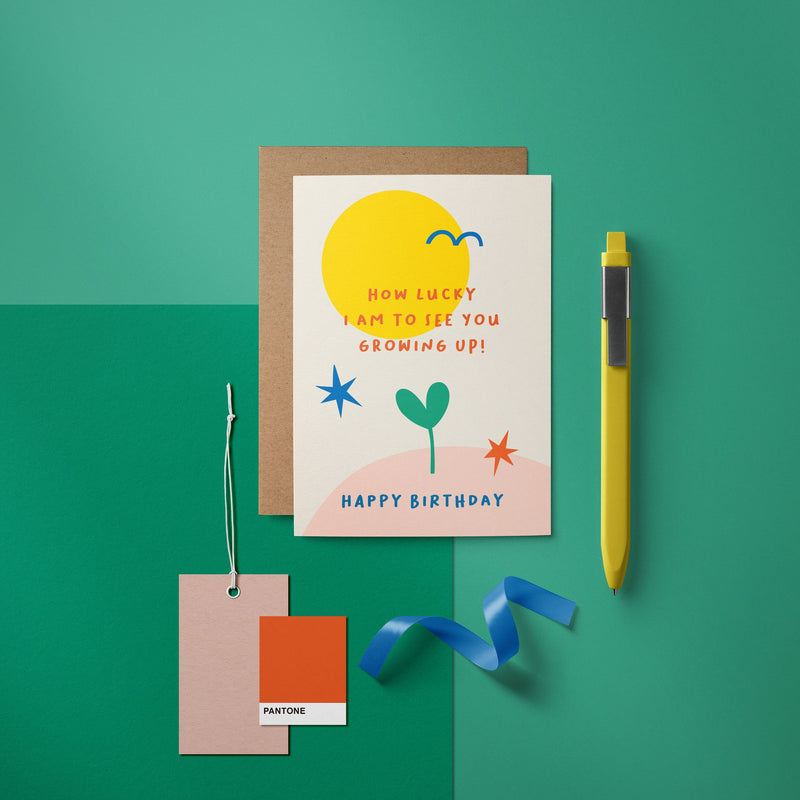 Birthday Card with yellow sun, blue bird, green plant, red and blue stars and a text that says How lucky I am to see you growing up