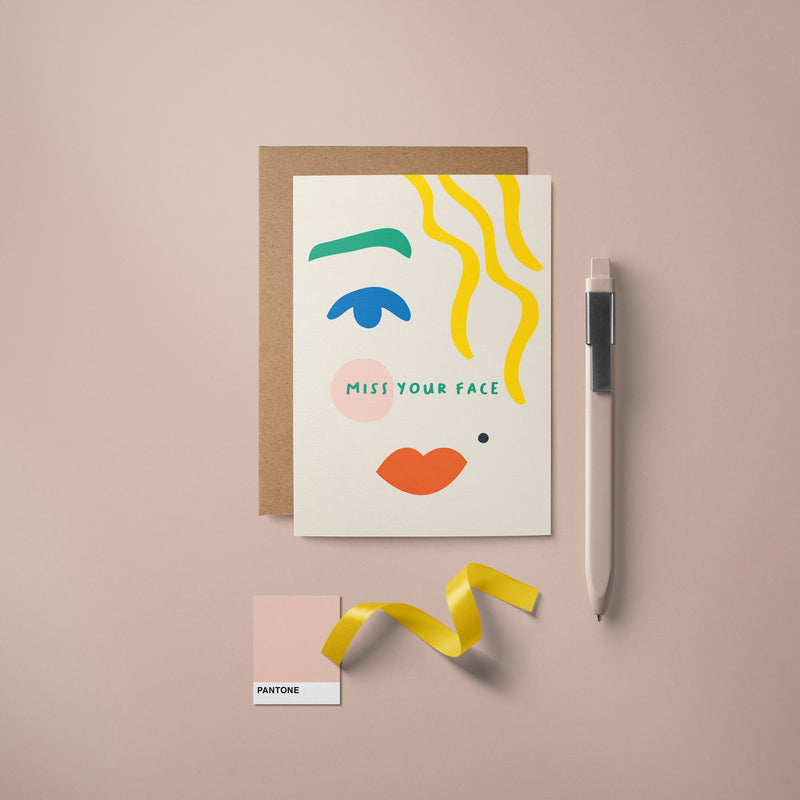 Greeting card with blue eye, green brow, red lips, yellow hair and a text that says Miss your face