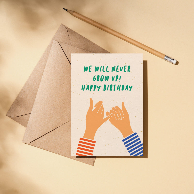 Birthday card with two hands creating gesture of promise with little fingers and a text that says we will never grow up happy birthday
