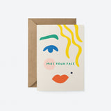Greeting card with blue eye, green brow, red lips, yellow hair and a text that says Miss your face