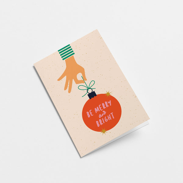 christmas card with a hand holding red christmas tree ornament and a text in it that says be merry and bright
