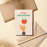 Birthday card with a hand holding a glass of wine and a text that says Cheers! Happy Birthday