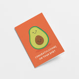 New baby greeting card with a green avocado and a its brown seed as a baby and a text that says congratulations on your baby