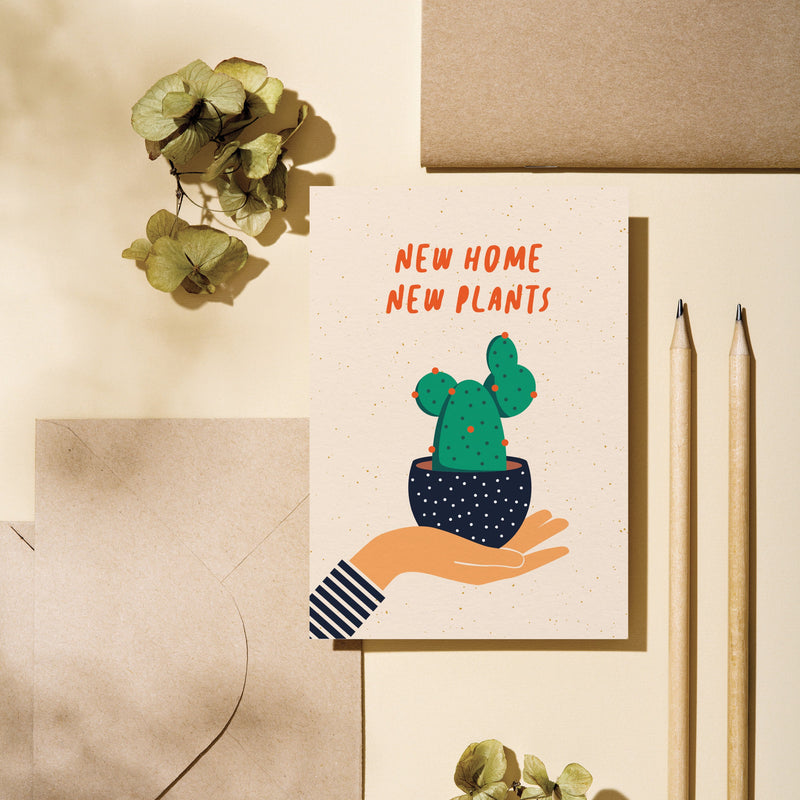 housewarming card with a hand holding a black flowerpot with a cactus in it and a text that says new home new plants
