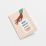 thank you card with a hand holding a white paper with a text in it that says Merci, Gracias, Danke 
