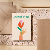 Thinking of you card with a hand holding red tulip and a text that says thinking of you